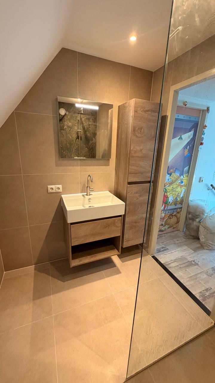 Badkamer op zolder met beige tegels, houten wastafelmeubel en inloopdouche